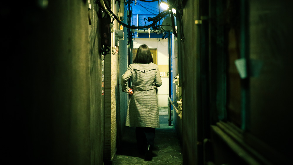Night photo of a woman walking down a narrow alley