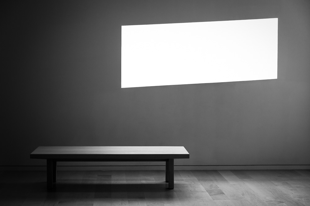 Black and white photo of a gallery bench beneath an illuminated wall panel